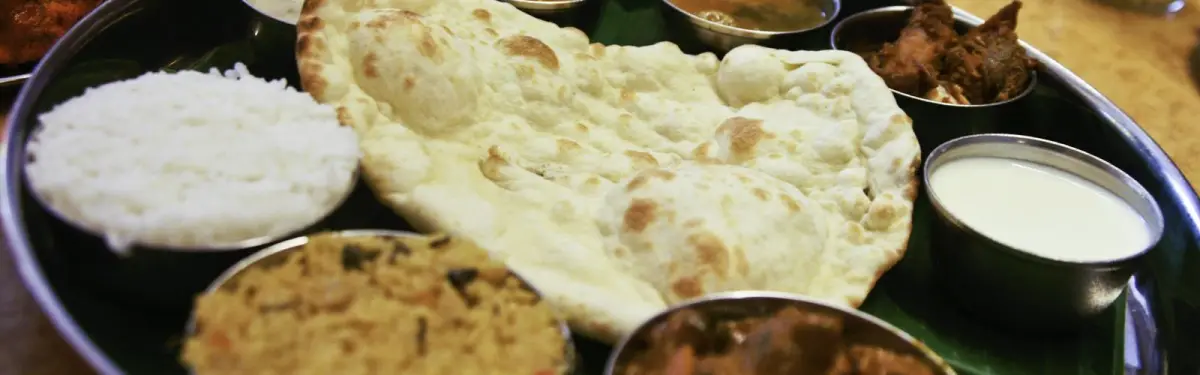 Thali-Platte mit frisch gebackenem Naan, Basmatireis, Raita und mehreren Curry-Schälchen aus Edelstahl